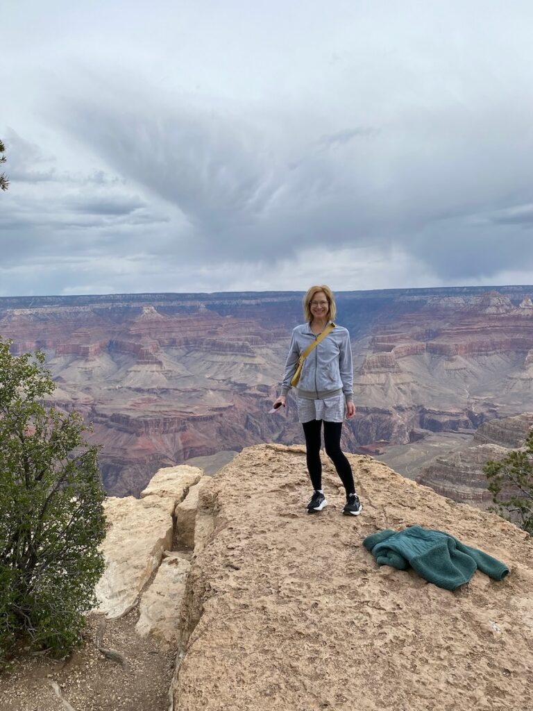 woman smiling and standing on rock in front of Grand Canyon